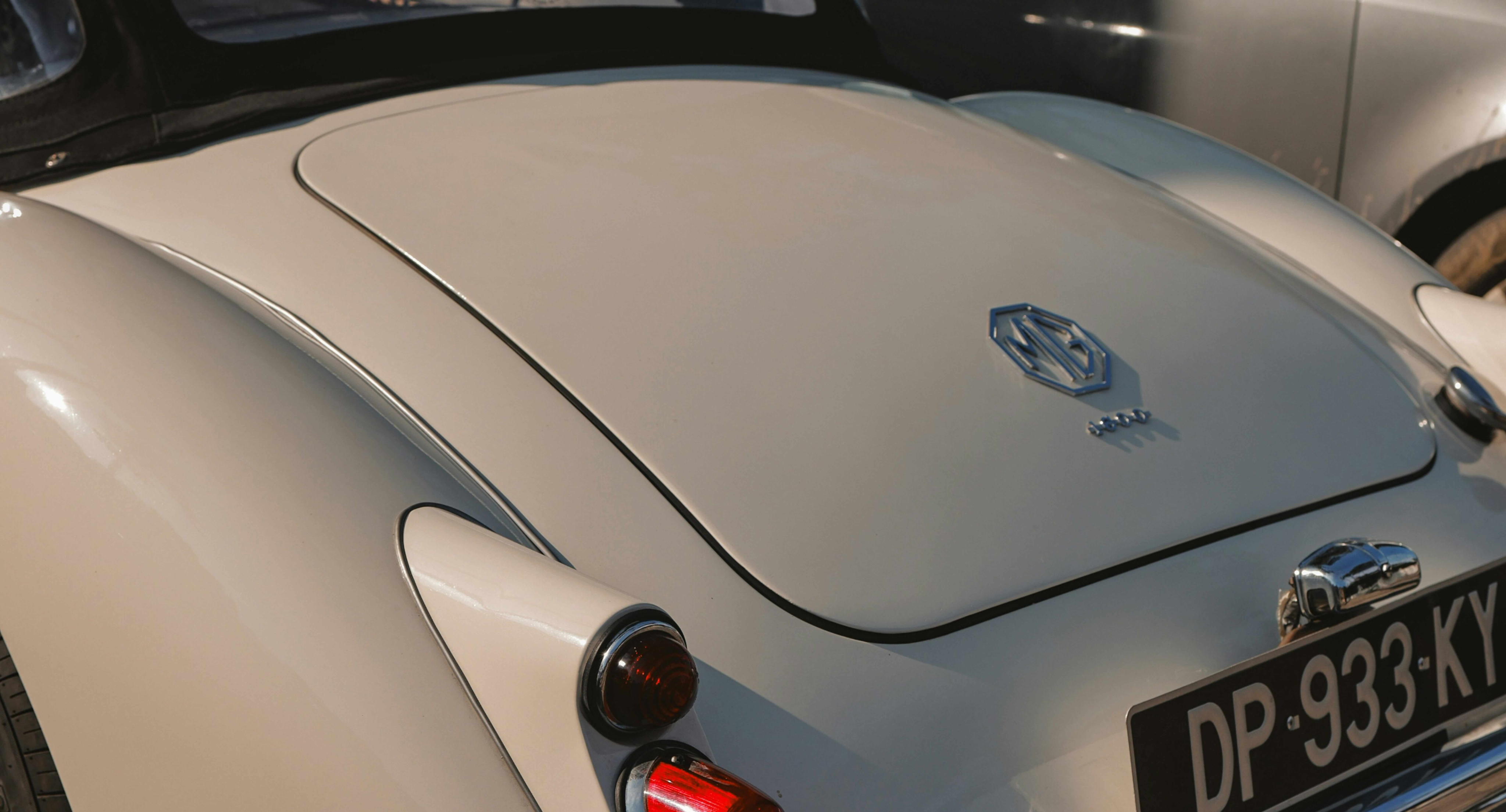 A close-up of the rear of a vintage car, featuring a sleek, cream-colored body and an emblem on it.